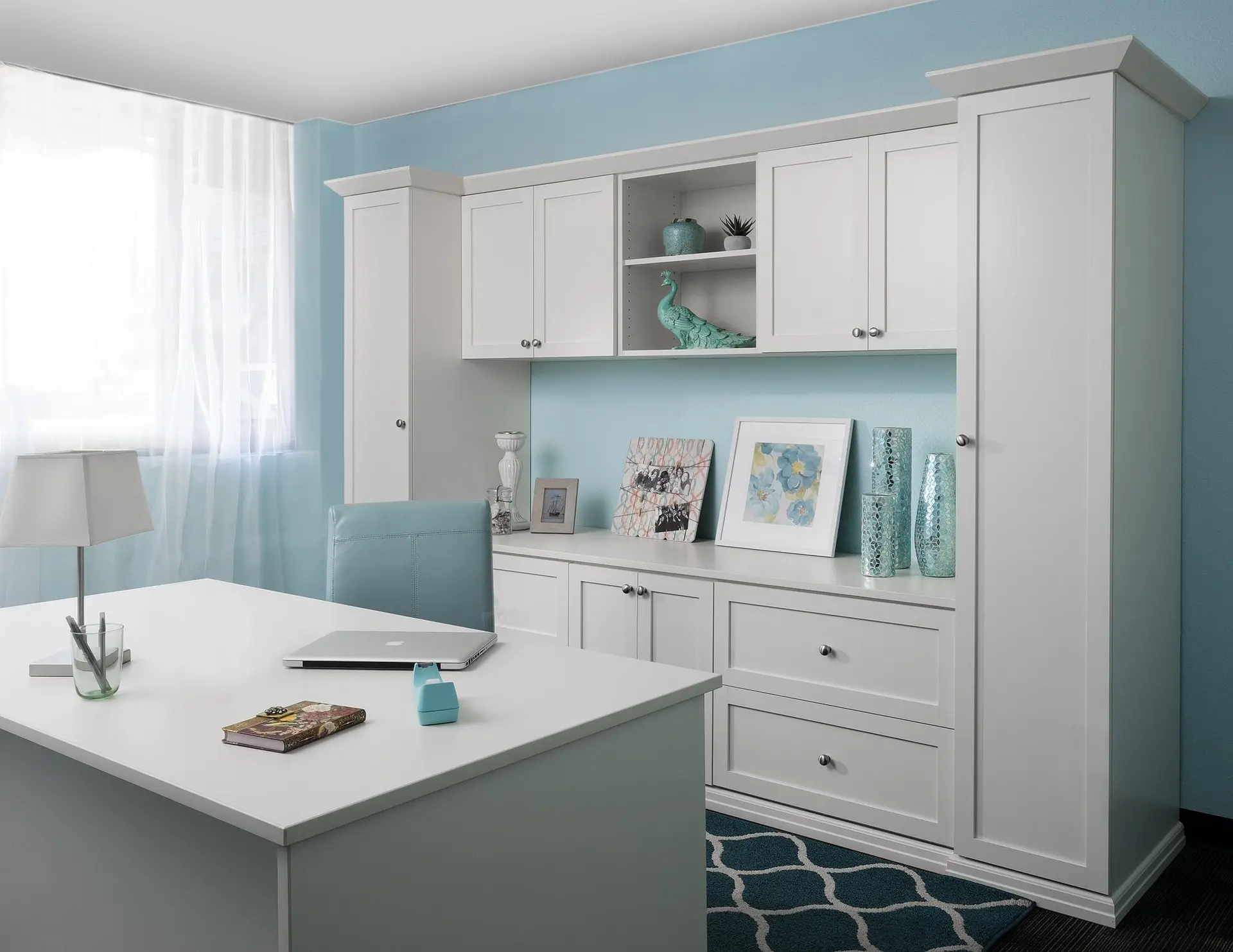 Antique white custom built in office desk with upper storage units against a teal accent wall