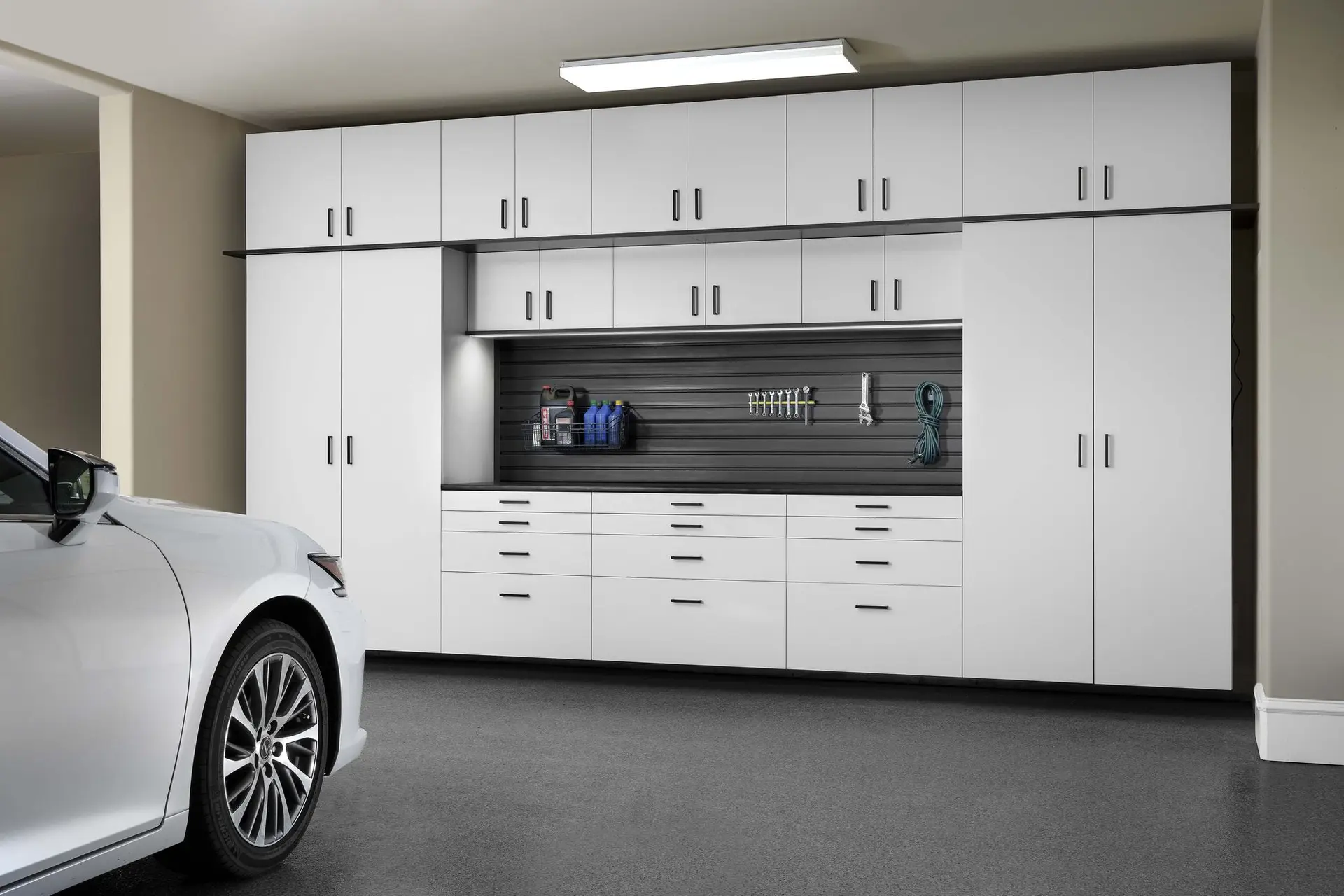 Garage tool organization setup with white cabinetry and a slatwall tracking system